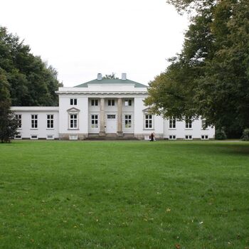 Ein großes, weißes Haus mit einem gepflegten Garten im Vordergrund.