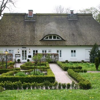 Ein weißes Haus mit einem Reetdach vor einem klaren blauen Himmel